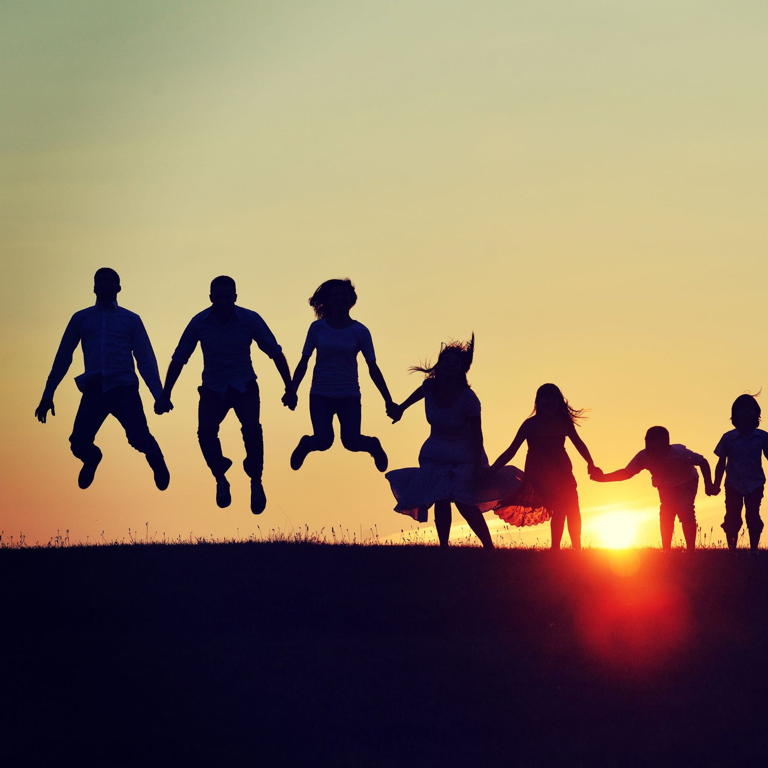 Silhouettes of people jumping together with the sunset in the background.