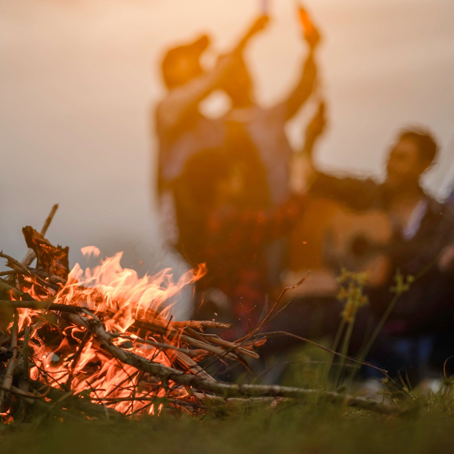 People playing guitar by a bonfire at sunset.