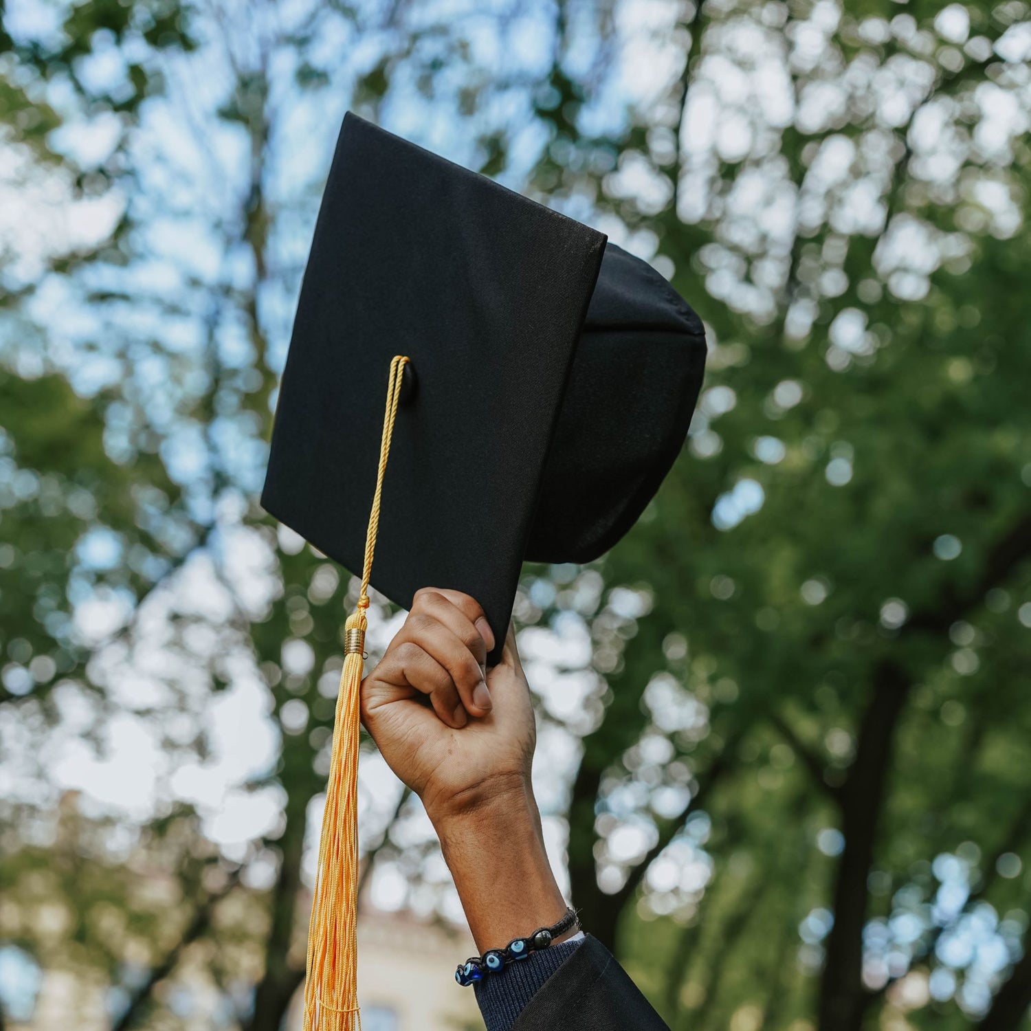 Graduation cap held by a hand with trees in the background