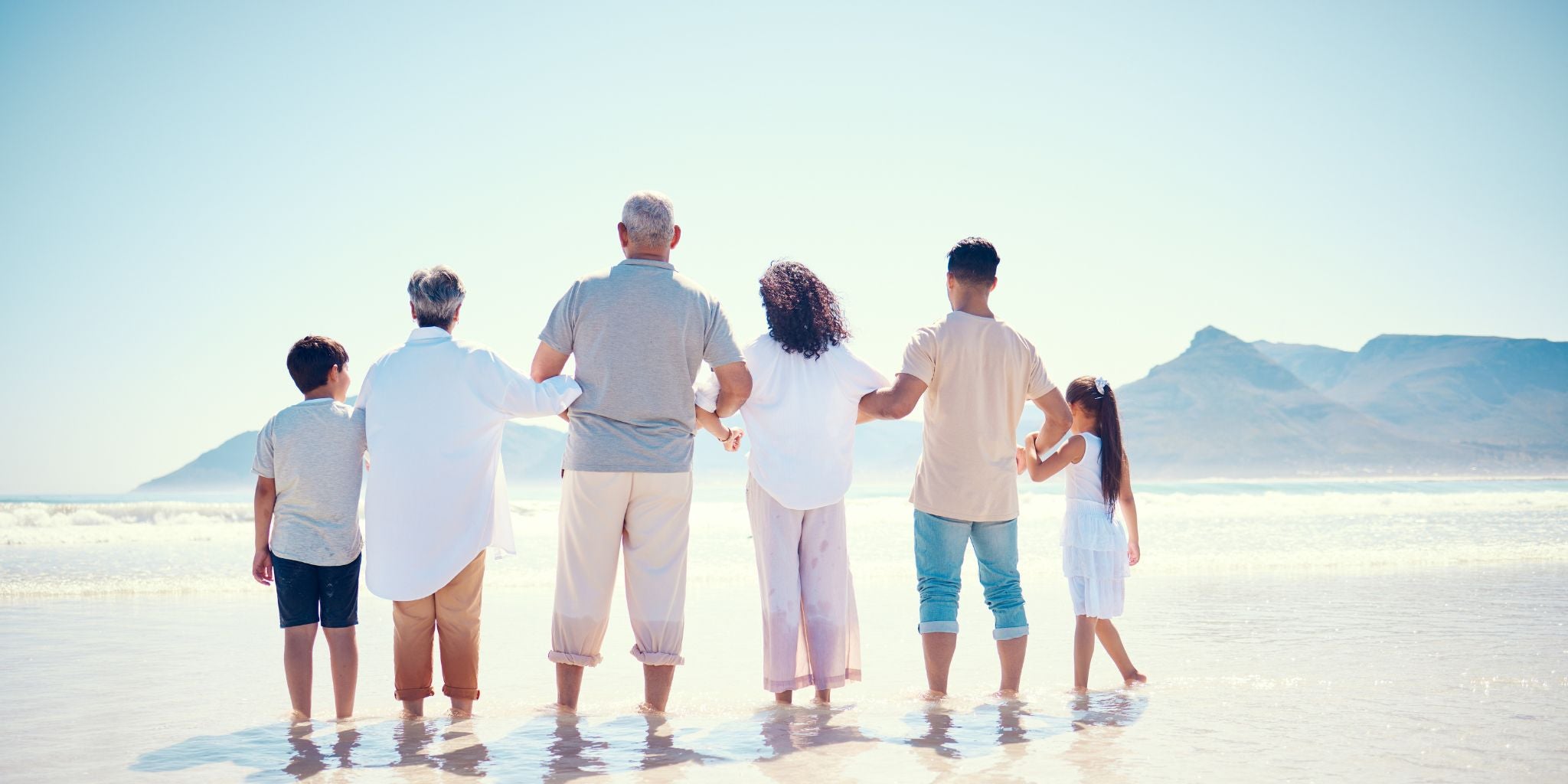 Family of six standing on a beach with mountains in the background