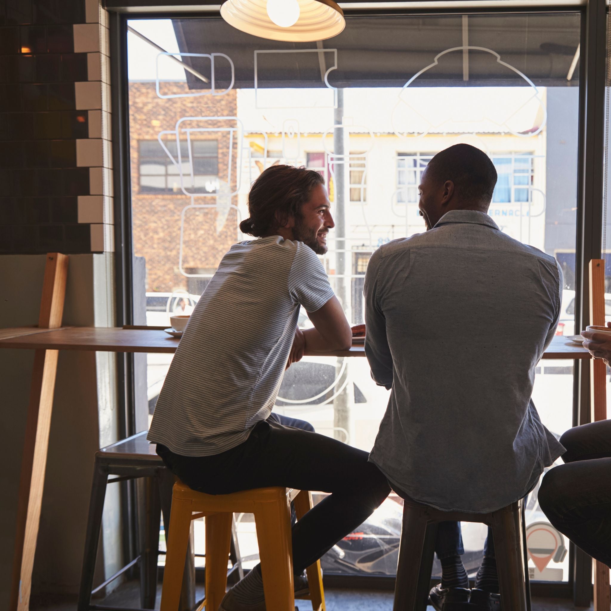 Two men sitting at a bar, viewed through a window.