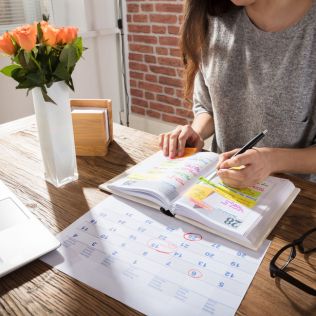Person sitting at a table with a planner and pen, surrounded by flowers and a vase.