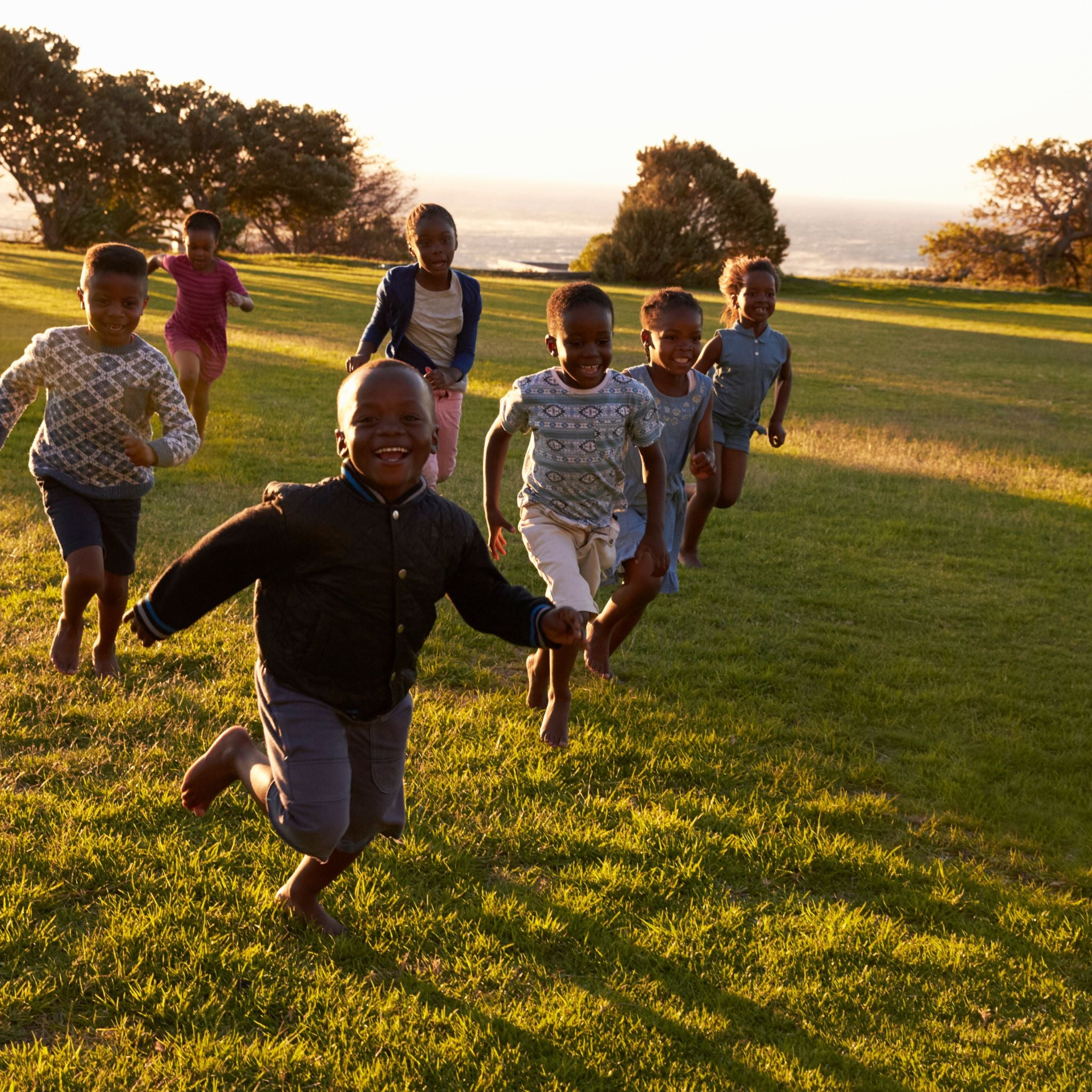 Children running on a grassy field at sunset.