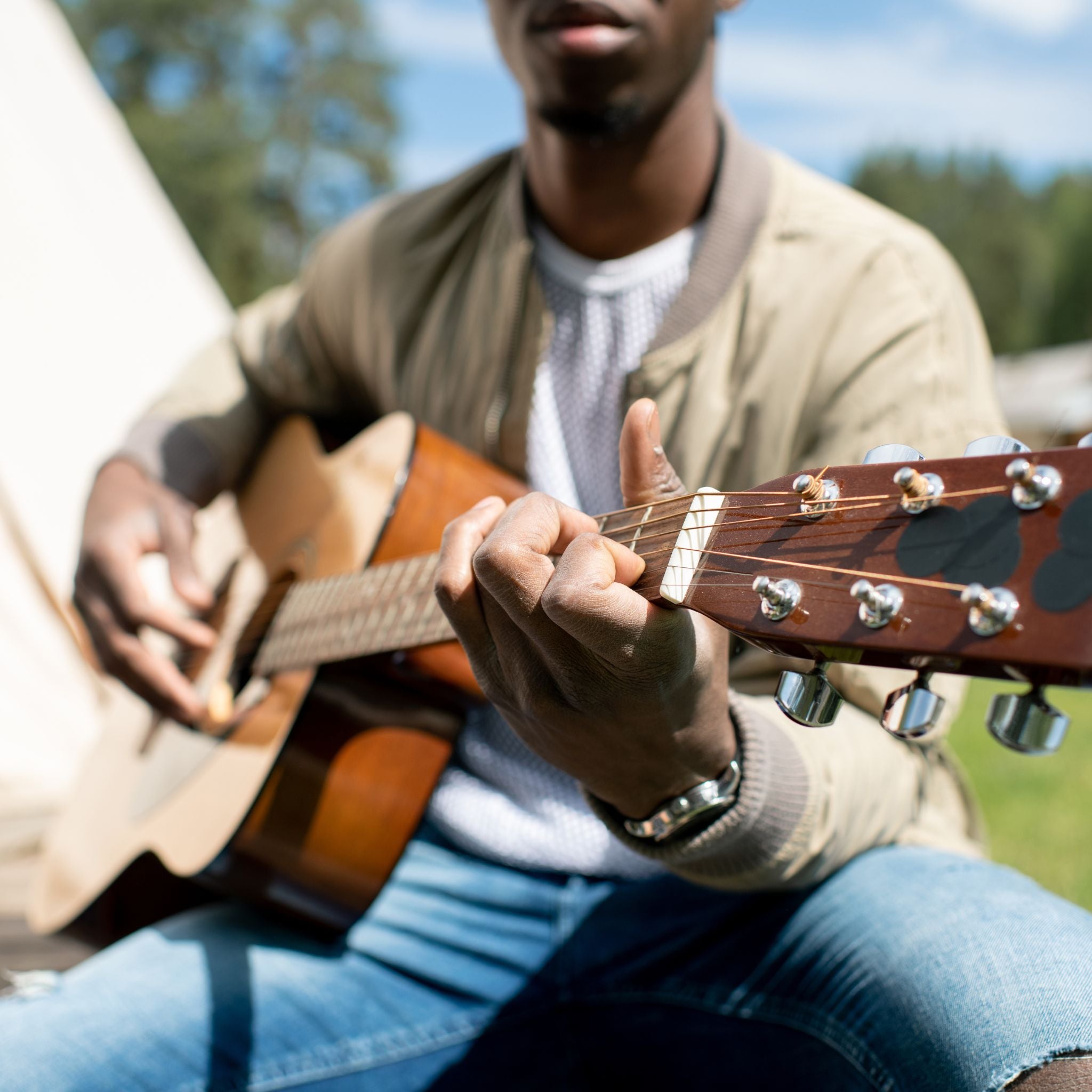 Person playing an acoustic guitar outdoors with trees in the background.