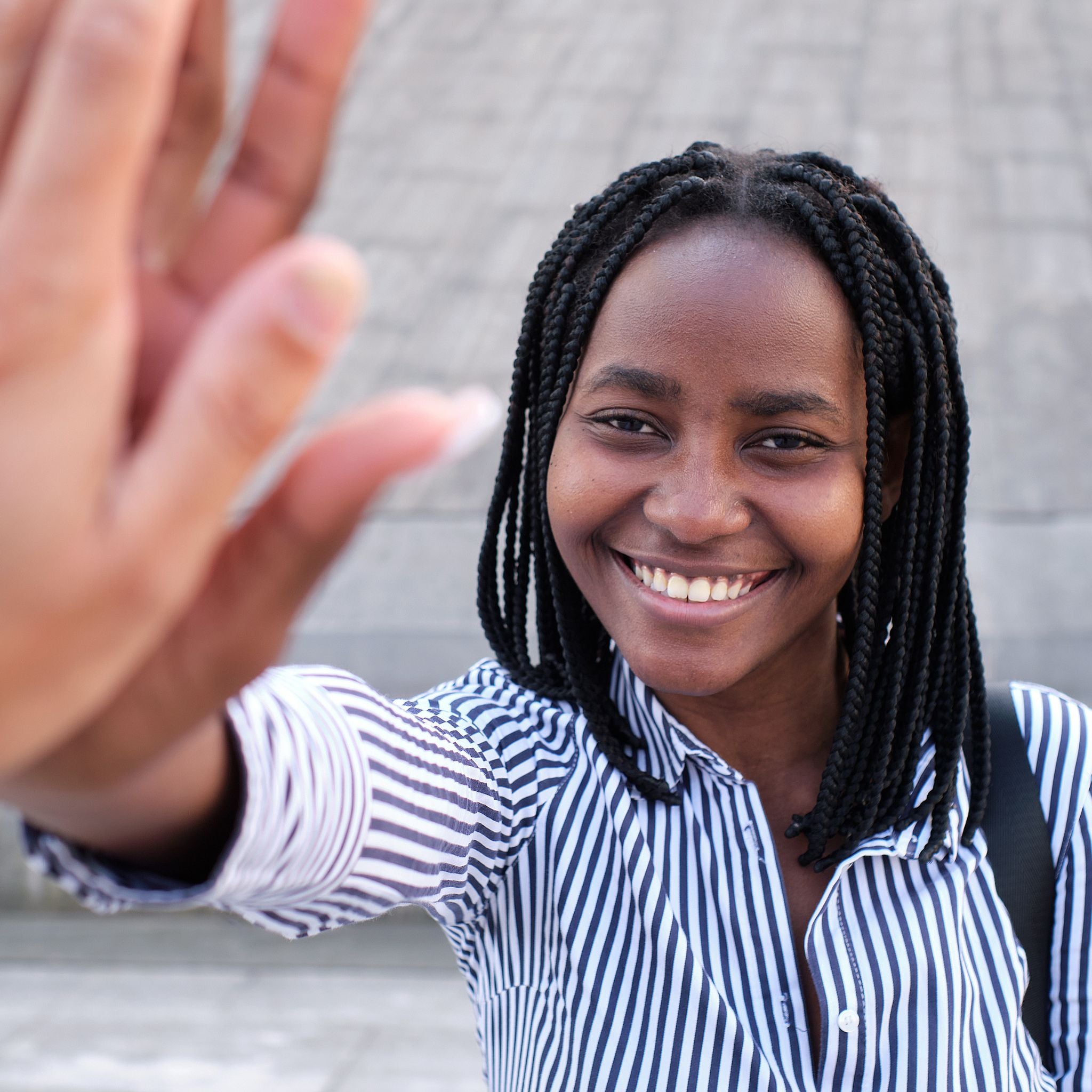 Person wearing a striped shirt with a blurred background high fiving a friend.